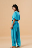 blauwe-massika-jumpsuit-met-kruishals-elastische-tailleband-korte-mouwen-grace-and-mila-model-zijaanzicht-1