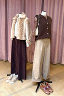 Twee staande outfits in een kledingwinkel: links een bontjasje met hertenmotief en donkere broek, rechts een bruin gilet met zandkleurige pantalon.