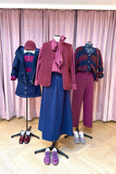 Drie etalagepoppen in paarse en blauwe tinten: links een blauw jack met jeansrokje, midden een geruite strikblouse met bordeaux teddy gilet en blauwe rok, rechts een gestreepte fluffy vest met paarse broek.