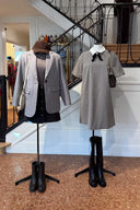 Twee etalagepoppen met herfst- en wintermode van Sienna voor een binnentrap. Links: een outfit met een grijze blazer, een donkere top, een zwarte spijkerrok met knopen, een bruine corduroy pet en een lichte crossbodytas, afgewerkt met donkerbruine enkellaarsjes. Rechts: een fijn geruite jurk met korte mouwen, een contrasterende witte kraag met een zwarte strik en broche, gecombineerd met een donkerbruine schoudertas en hoge zwarte laarzen.