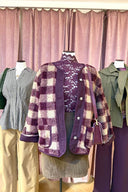 Medium shot van drie mannequins in winkeletalage: gecentreerd een geruit paars-beige teddy vest over paarse kantentop met corduroy rok en paars leren tasje.