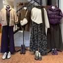 Winkeletalage in Antwerpen met vier mannequins voor een trap: een beige fleece jack op een paarse pantalon, een bruine corduroy jurk met tasje, een ecru gebreide trui op een camouflagebroek met groene sjaal, en een paarse puffer jas op een donkere broek met sneakers.