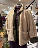 Close-up van een mannequin in een winkel: beige oversized teddy jack met legergroene voering en details, gedragen over een paarse kanten top met opstaande kraag en een gouden ketting.